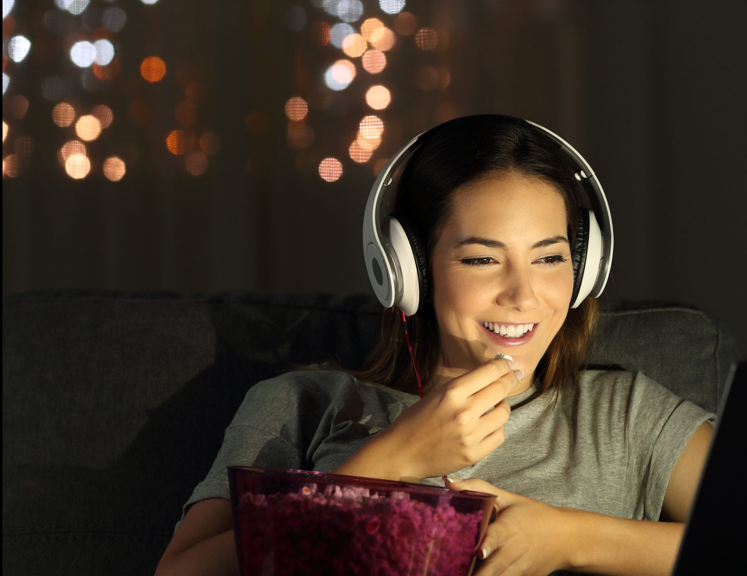 Single woman watching online tv in the night sitting on a couch in the living room at home