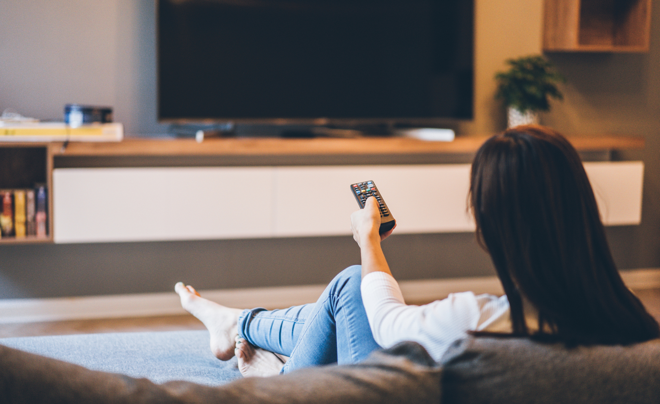 Woman watching TV, sitting on the sofa at home, back view