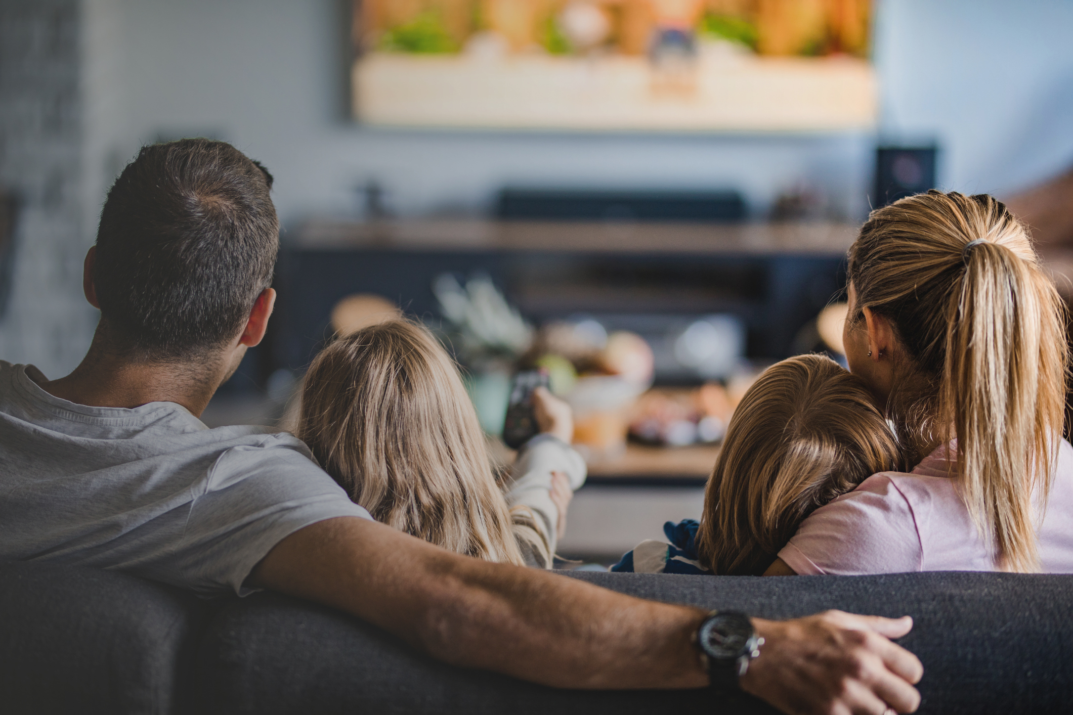 Back view of a relaxed family watching TV on sofa in the living room.