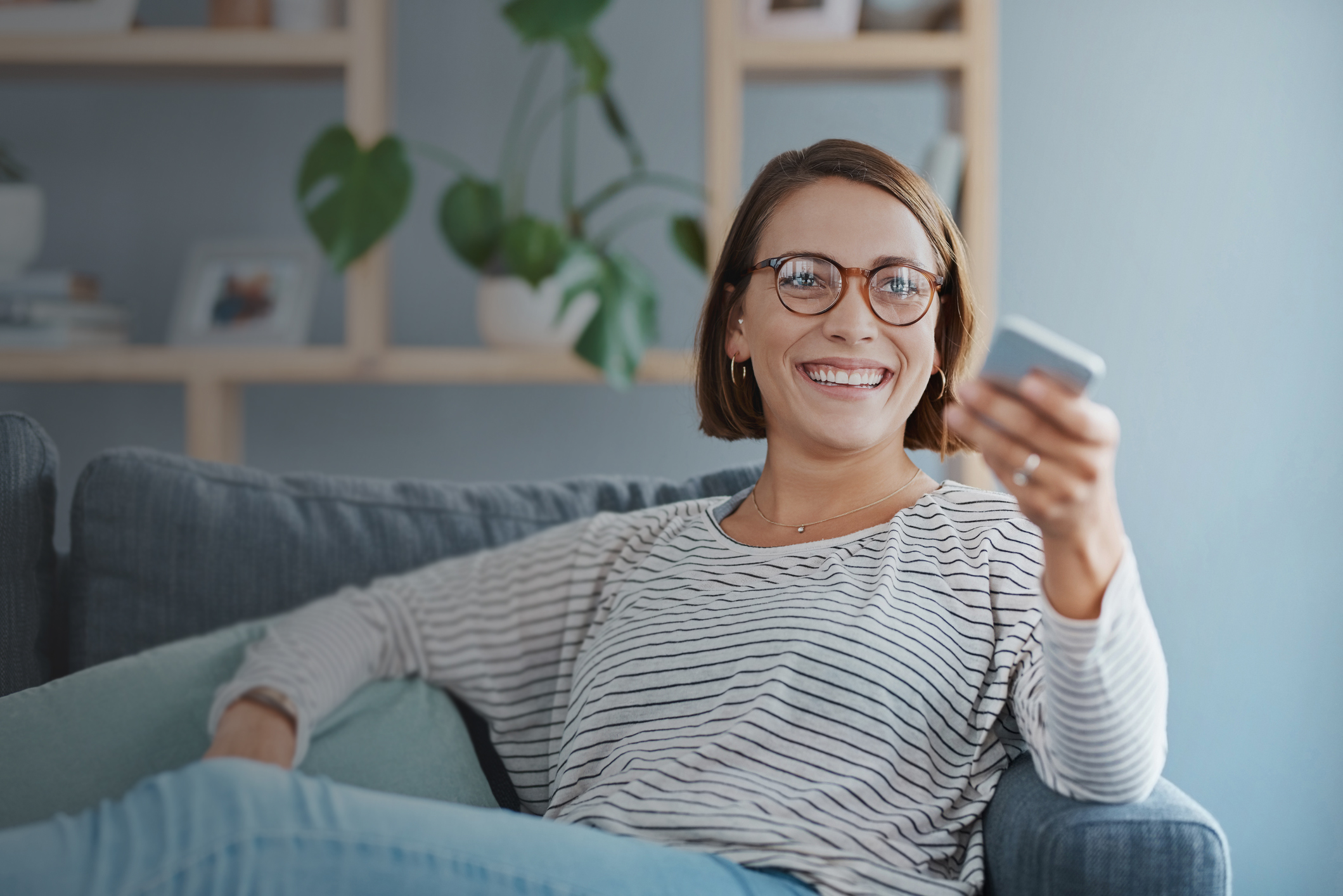Cropped shot of a happy young woman using the remote control on the sofa at home