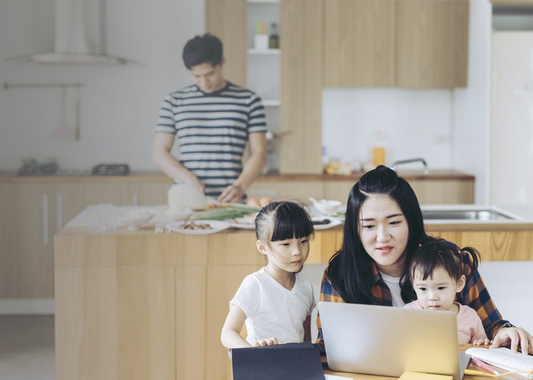 Mother taking care of children and trying to work and father cooking dinner for the family.