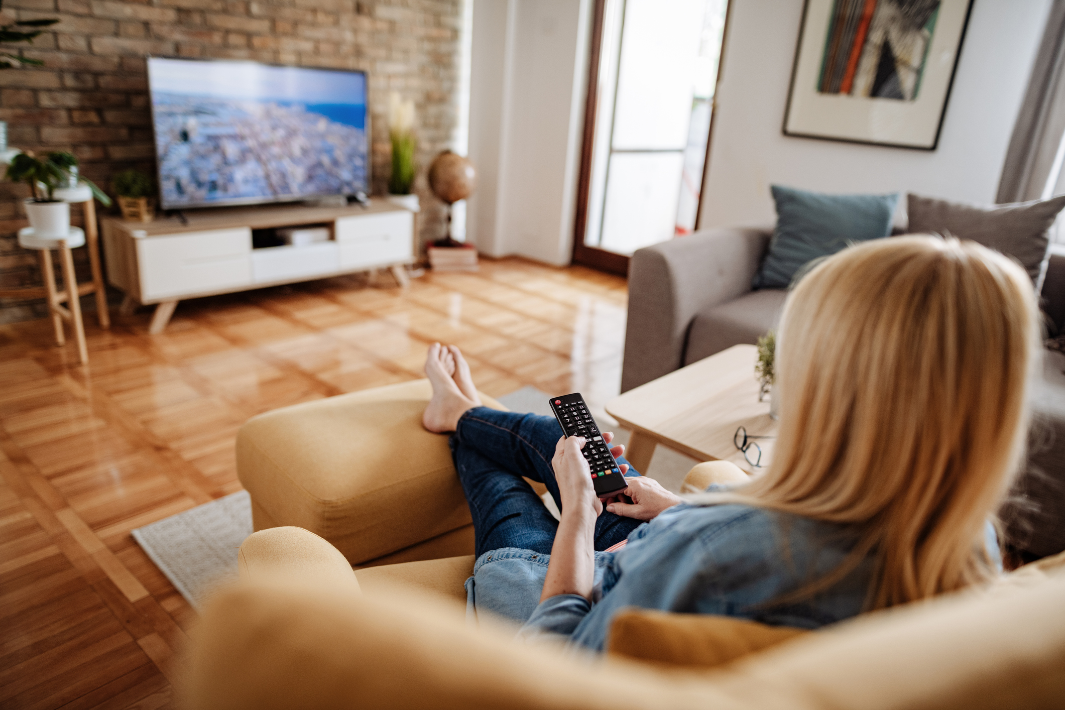 Caucasian blond hair woman, around 60 years old resting at home and watching TV