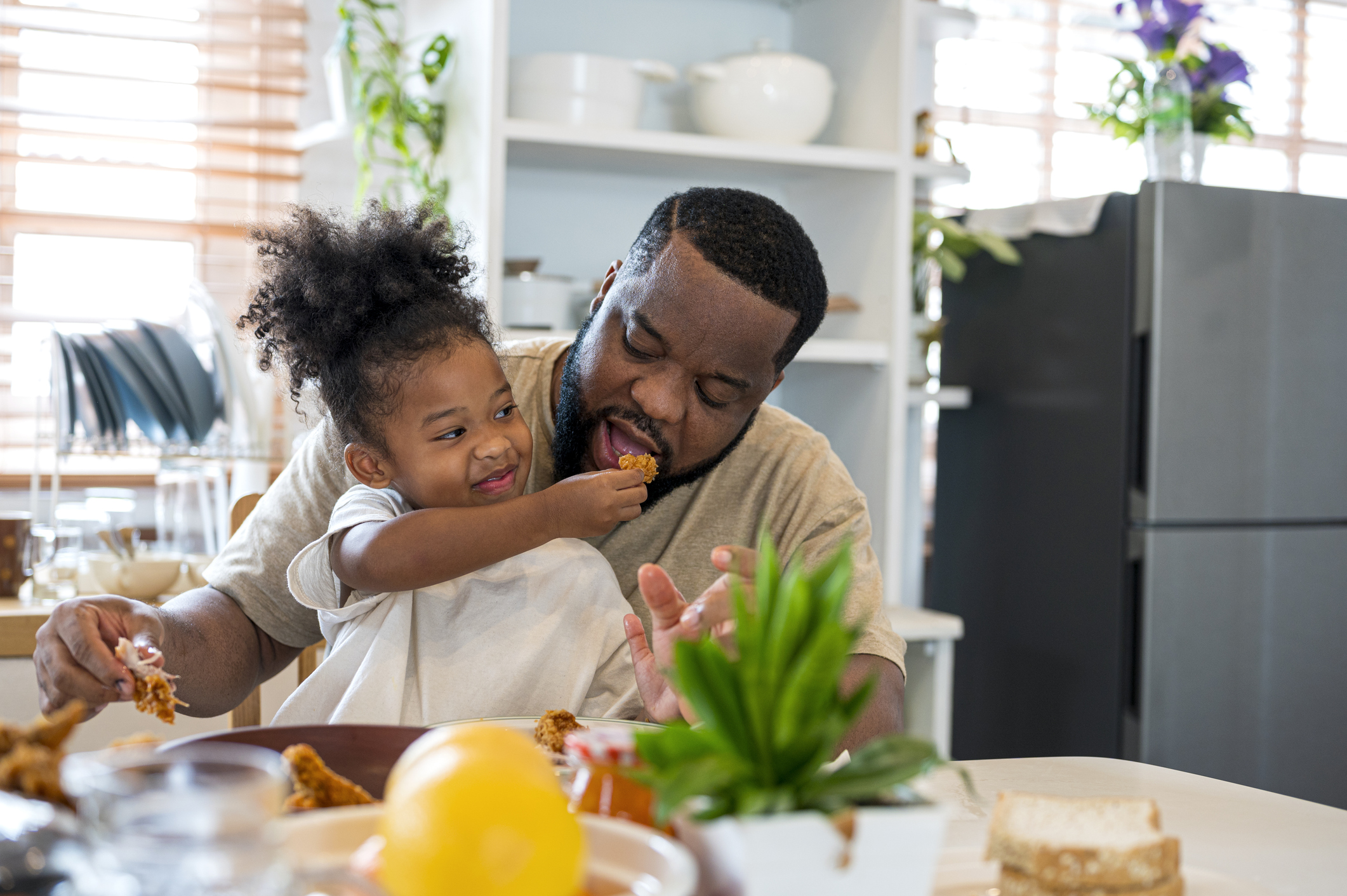 African Papa and daughter having lunch together.  They are enjoy eating a fired chicken meal at home.