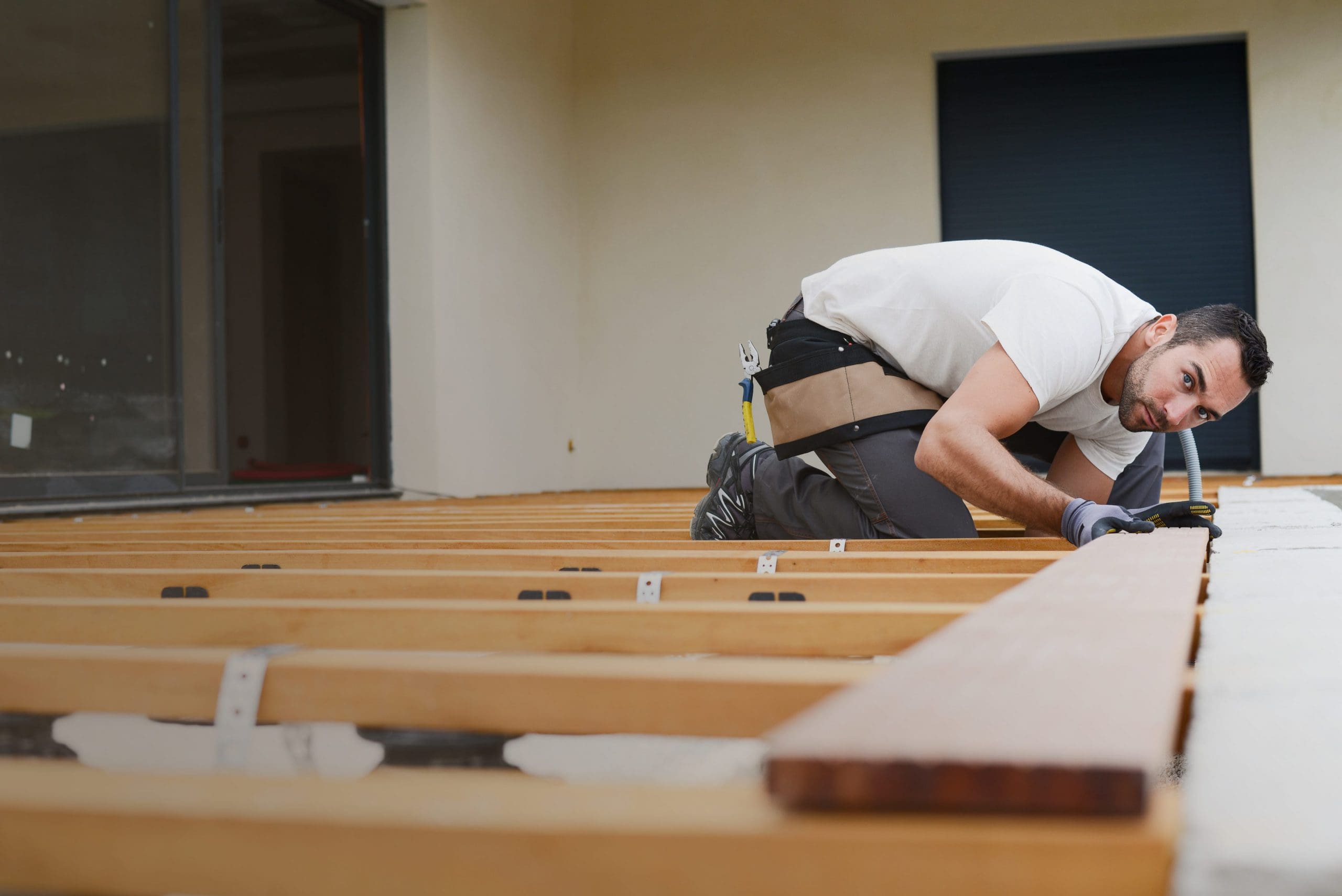 handsome young man carpenter installing a wood floor outdoor terrace in new house construction site