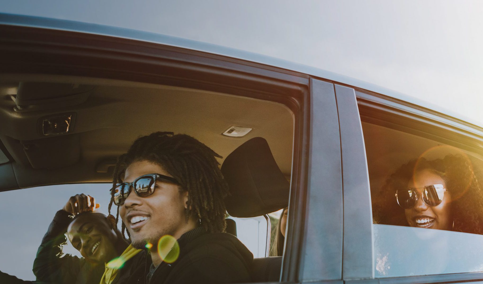 A smiling group of Generation Z young adults enjoy a road trip on a sunny day.  Mixed ethnic group.  Horizontal image with copy space.