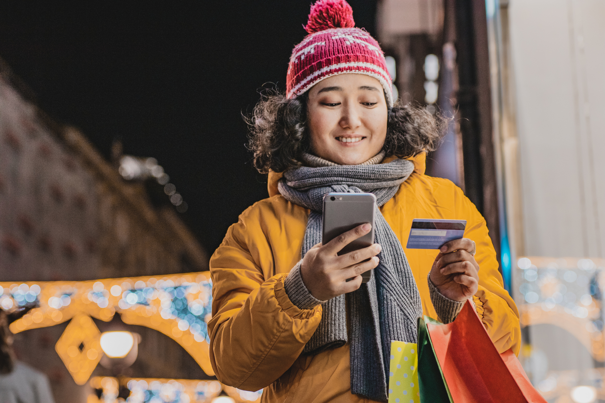 Young woman holding shopping bags and using mobile phone and credit card